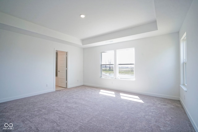 spare room featuring light carpet, baseboards, recessed lighting, and a raised ceiling