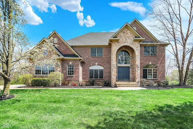 view of front of home with brick siding, a front lawn, roof with shingles, and stone siding