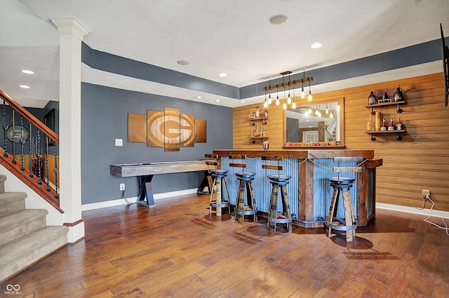 bar featuring baseboards, a bar, stairway, and hardwood / wood-style floors