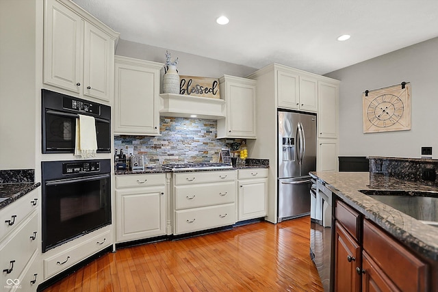 kitchen with tasteful backsplash, white cabinets, light wood finished floors, dark stone counters, and stainless steel appliances