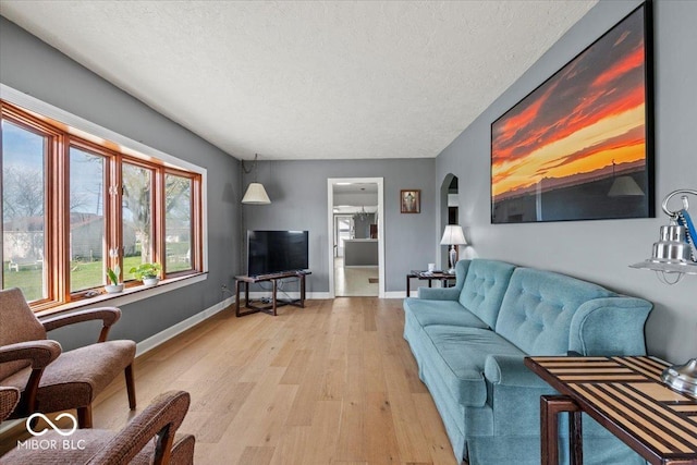 living room with a textured ceiling, baseboards, light wood finished floors, and arched walkways
