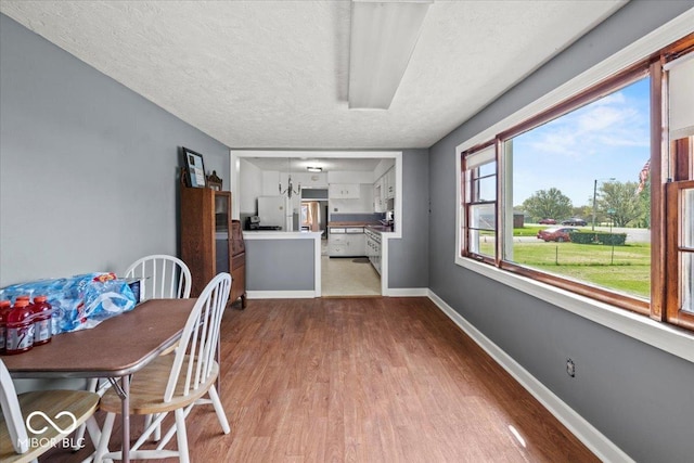 dining space with a textured ceiling, wood finished floors, and baseboards