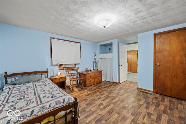 bedroom with a textured ceiling, wood finished floors, and baseboards