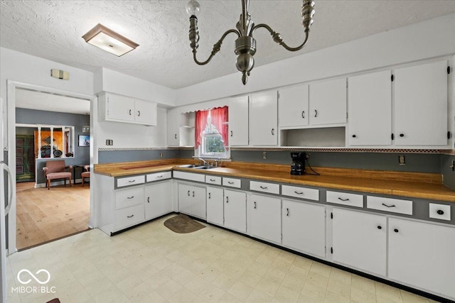 kitchen featuring an inviting chandelier, light floors, a sink, white cabinetry, and a textured ceiling