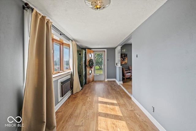 foyer with a wall unit AC, a textured ceiling, baseboards, and light wood-type flooring