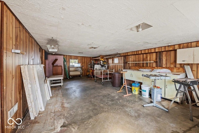 miscellaneous room with a textured ceiling, wooden walls, and unfinished concrete flooring