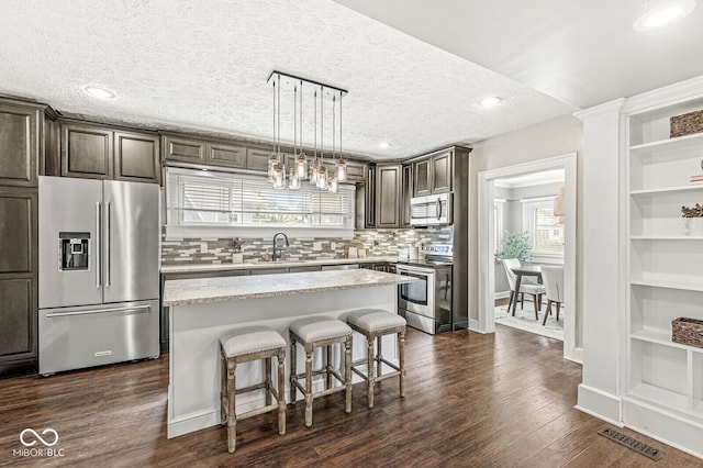 kitchen with decorative backsplash, a kitchen island, a breakfast bar, a sink, and stainless steel appliances