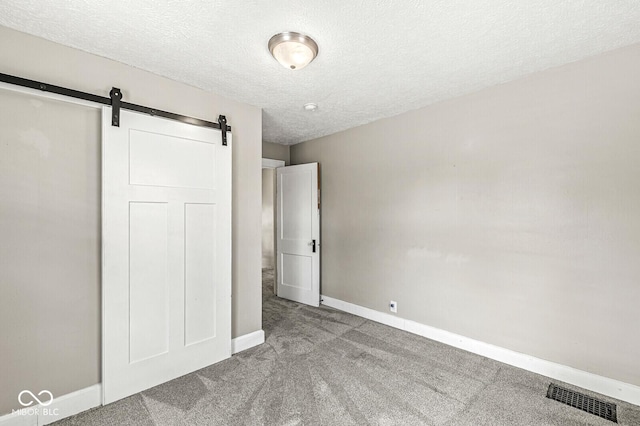 unfurnished bedroom featuring a barn door, carpet floors, a textured ceiling, baseboards, and visible vents