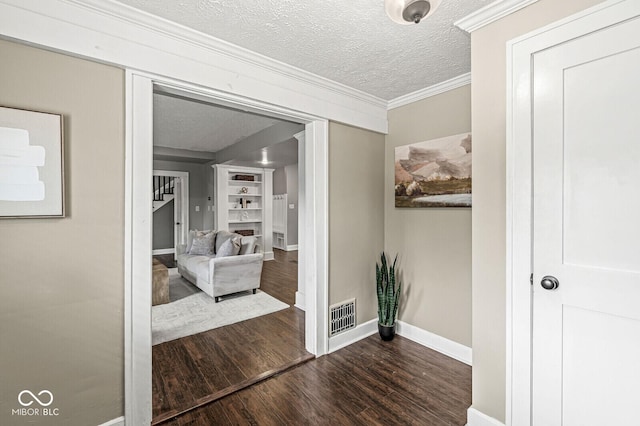 corridor with visible vents, crown molding, wood finished floors, baseboards, and a textured ceiling