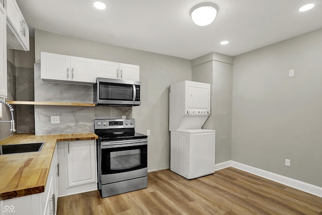 734 N Bradley Ave, Indianapolis, IN 46201 - kitchen featuring light wood finished floors, butcher block counters, white cabinetry, stacked washer and clothes dryer, and appliances with stainless steel finishes