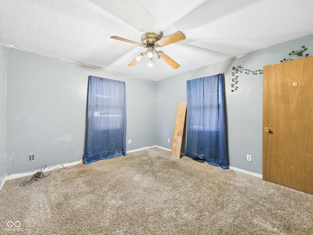 carpeted empty room featuring a ceiling fan and baseboards