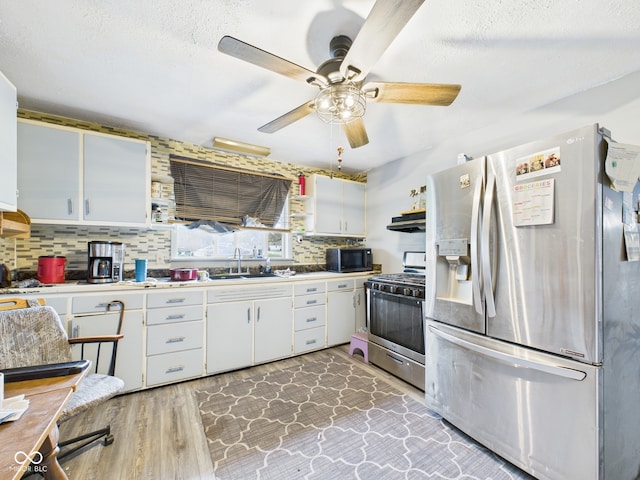 kitchen with a sink, ceiling fan, stainless steel appliances, light countertops, and white cabinetry
