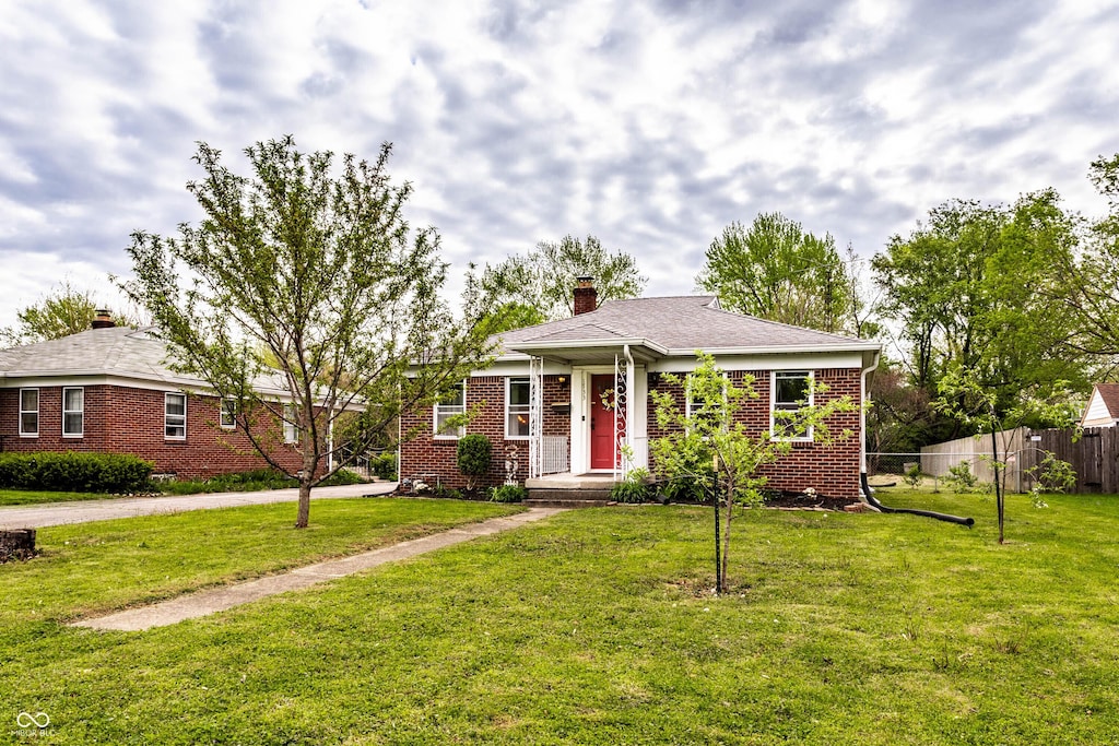 view of front of property with a front lawn, fence, a chimney, brick siding, and driveway