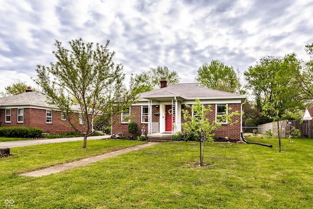 view of front of property with a front lawn, fence, a chimney, brick siding, and driveway