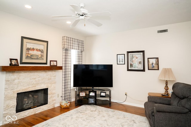 living room with visible vents, baseboards, wood finished floors, a ceiling fan, and a stone fireplace