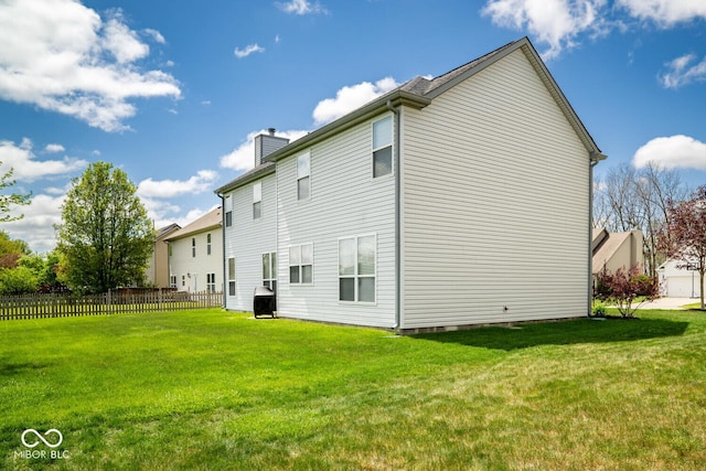 rear view of property with a yard, a chimney, and fence