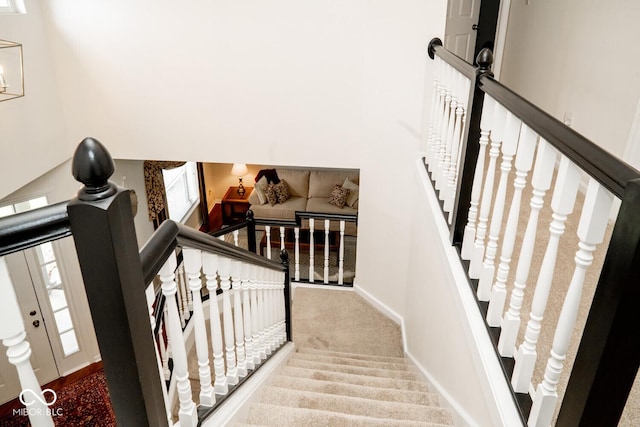 staircase with a towering ceiling, carpet floors, and baseboards