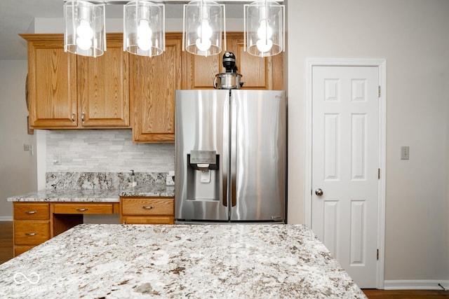kitchen featuring pendant lighting, baseboards, light stone countertops, stainless steel fridge, and backsplash