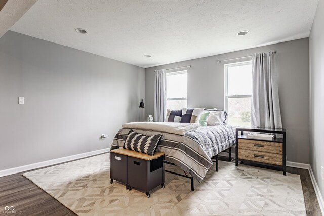 bedroom with baseboards, light wood-type flooring, a textured ceiling, and recessed lighting