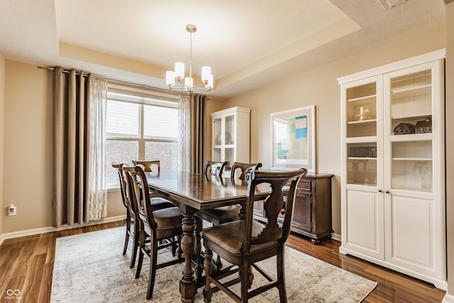dining space with dark wood finished floors, baseboards, a raised ceiling, and a notable chandelier
