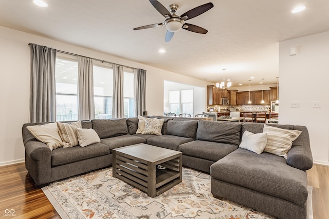 living room featuring recessed lighting, baseboards, light wood-style flooring, and ceiling fan with notable chandelier