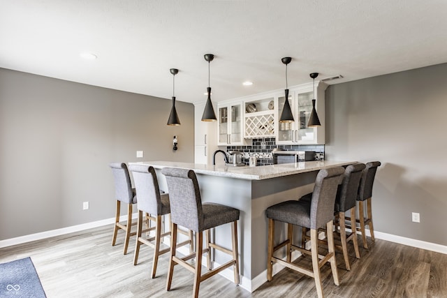 kitchen featuring a kitchen breakfast bar, backsplash, wood finished floors, and baseboards