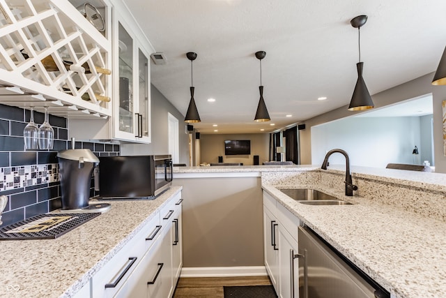 kitchen featuring stainless steel dishwasher, a sink, light stone counters, and decorative backsplash
