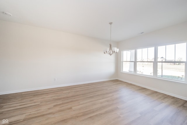 unfurnished room featuring light wood-style floors, baseboards, and a notable chandelier