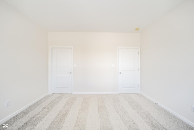 spare room with baseboards and light carpet