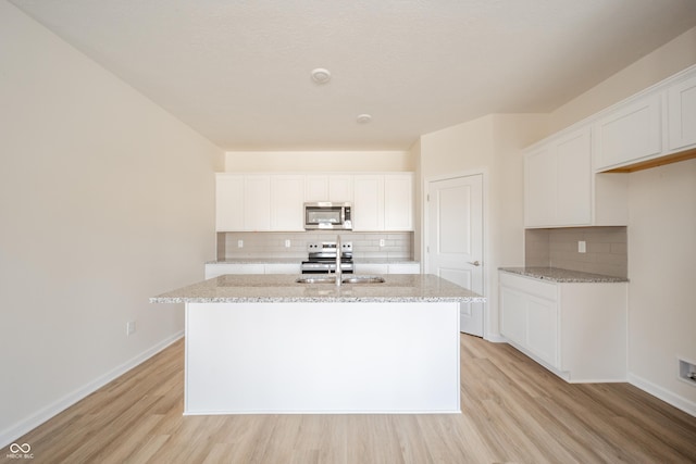 kitchen with backsplash, appliances with stainless steel finishes, a center island with sink, a sink, and light wood-style floors