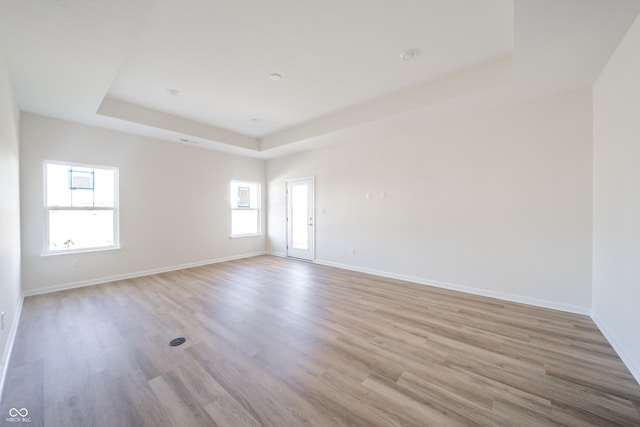 empty room with a tray ceiling, baseboards, and light wood-style floors
