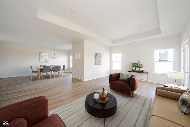 living area with baseboards, a tray ceiling, a healthy amount of sunlight, and light wood-style flooring