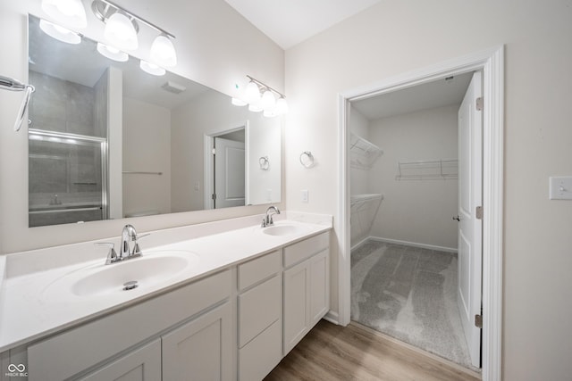 bathroom featuring double vanity, a sink, a shower with shower door, and wood finished floors