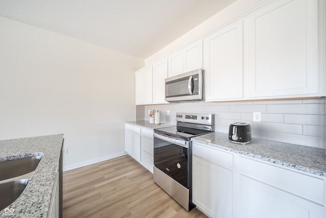 kitchen featuring decorative backsplash, light wood-style floors, baseboards, white cabinets, and appliances with stainless steel finishes