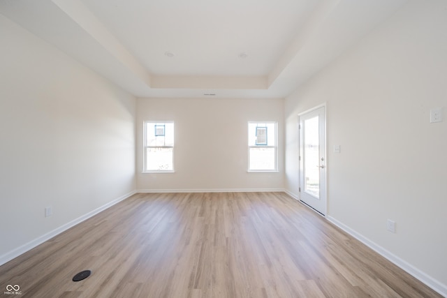 spare room with light wood-style floors, a raised ceiling, and baseboards