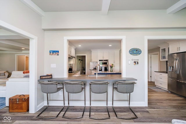 kitchen with dark wood finished floors, stainless steel appliances, dark countertops, a breakfast bar area, and white cabinetry