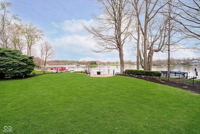 view of yard featuring fence, a water view, and a boat dock