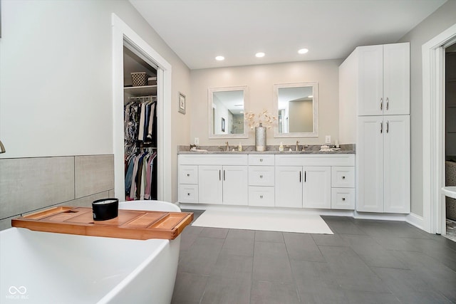 full bathroom with a sink, double vanity, a freestanding bath, a spacious closet, and recessed lighting