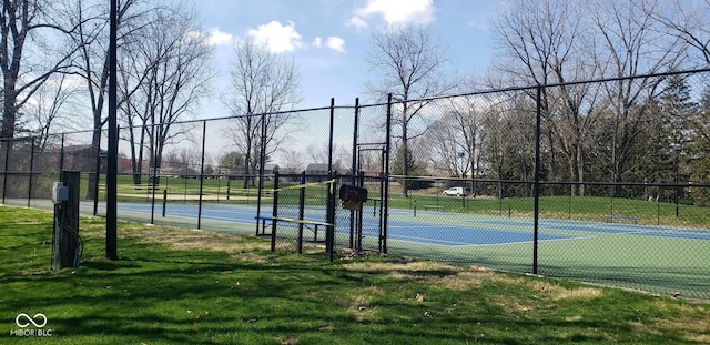 view of tennis court featuring a lawn and fence