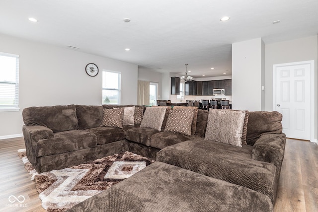 living area with a healthy amount of sunlight, recessed lighting, wood finished floors, and an inviting chandelier