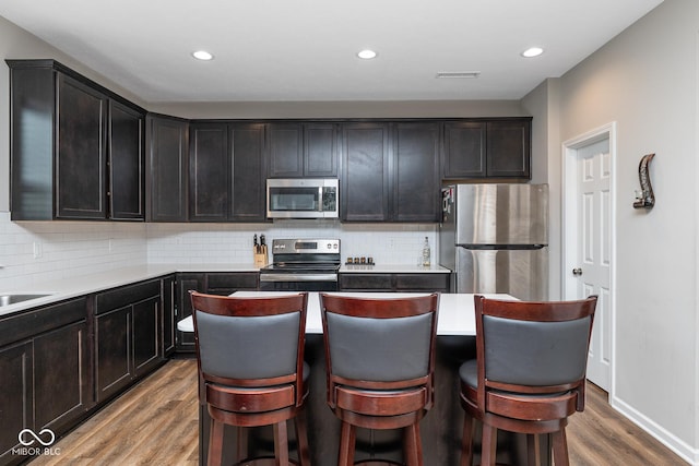 kitchen with decorative backsplash, stainless steel appliances, a center island, recessed lighting, and wood finished floors