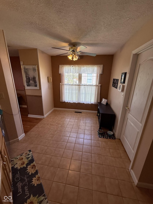 interior space with visible vents, a ceiling fan, light tile patterned floors, baseboards, and a textured ceiling