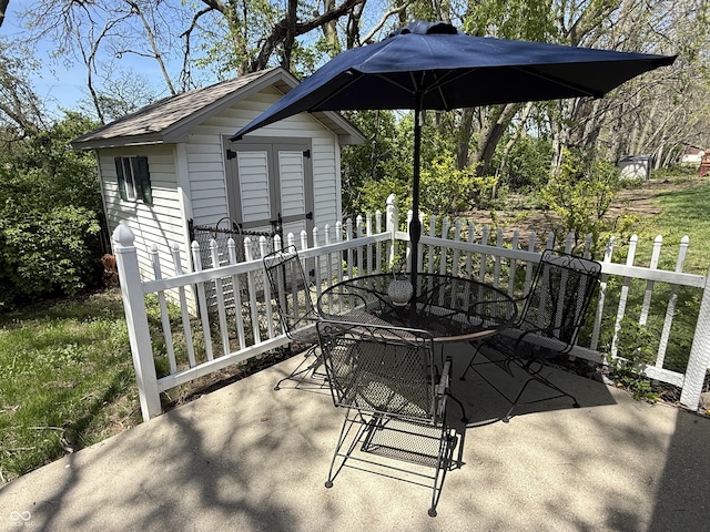 view of patio featuring a storage unit, outdoor dining space, an outbuilding, and fence