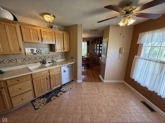 kitchen featuring stainless steel dishwasher, a sink, visible vents, backsplash, and light countertops