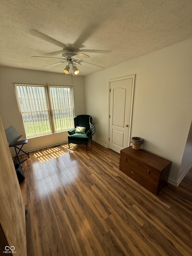 living area featuring wood finished floors, a textured ceiling, baseboards, and ceiling fan