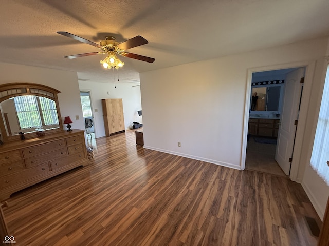 unfurnished bedroom featuring dark wood-type flooring, baseboards, ceiling fan, and ensuite bathroom
