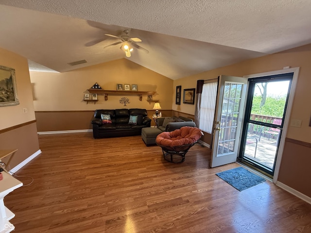 living room with a textured ceiling, visible vents, lofted ceiling, a ceiling fan, and wood finished floors