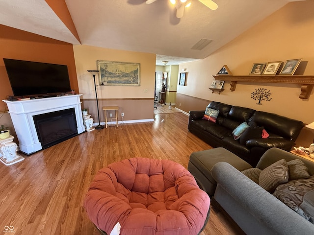 living area featuring a glass covered fireplace, lofted ceiling, wood finished floors, and ceiling fan