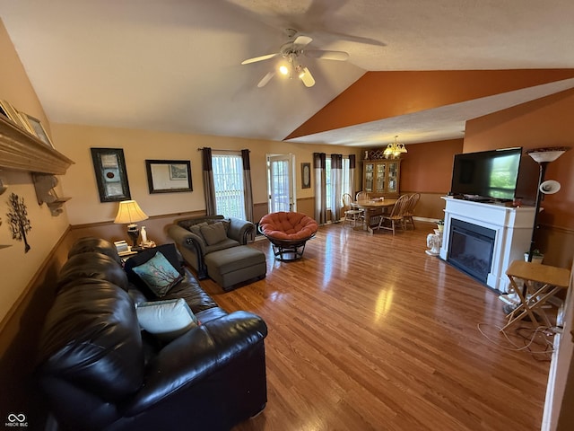 living room with vaulted ceiling, baseboards, a glass covered fireplace, a ceiling fan, and wood finished floors