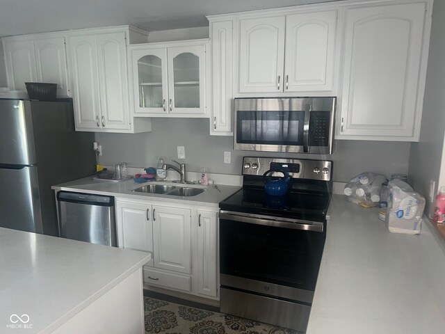 7206 Halden Pl, Indianapolis, IN 46214 - kitchen with appliances with stainless steel finishes, a sink, white cabinetry, light countertops, and glass insert cabinets